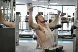 A man using a lat pulldown machine in a gym, performing a wide-grip back exercise while seated.