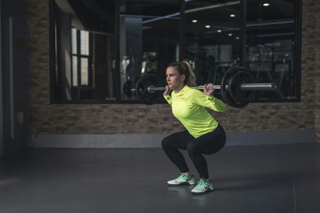 A woman working out her glutes by doing barbell squats in a gym, exemplifying a routine that could be part of a weekly exercise plan targeting the gluteal muscles.