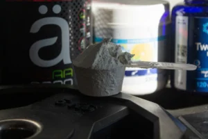 Measuring scoop of pre-workout powder on a weight plate with supplement containers in the background