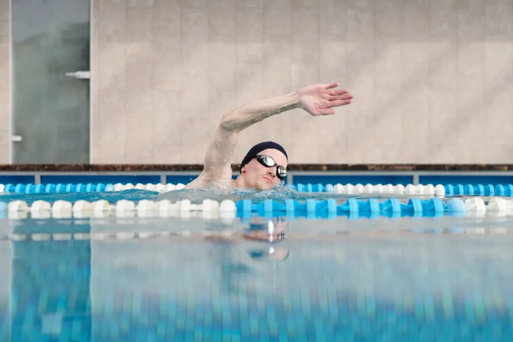 swimming calories – male swimmer doing freestyle stroke in indoor pool for fitness