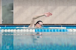 swimming calories – male swimmer doing freestyle stroke in indoor pool for fitness