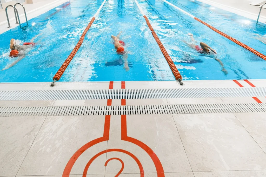 Swimming laps in a pool – three athletes swimming freestyle in an indoor pool for weight loss