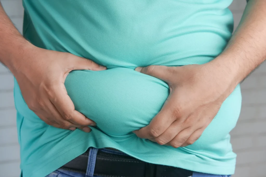 Visceral fat – close-up of hands gripping abdominal belly fat for body composition assessment
