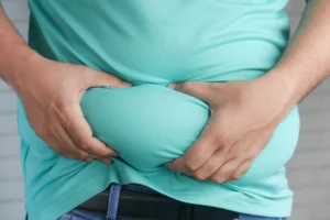 Visceral fat – close-up of hands gripping abdominal belly fat for body composition assessment