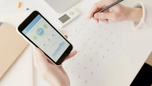 Hands using a smartphone to track fitness stats while planning a workout calendar