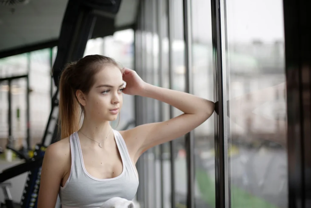 Woman standing pensively near a gym window, illustrating gym anxiety