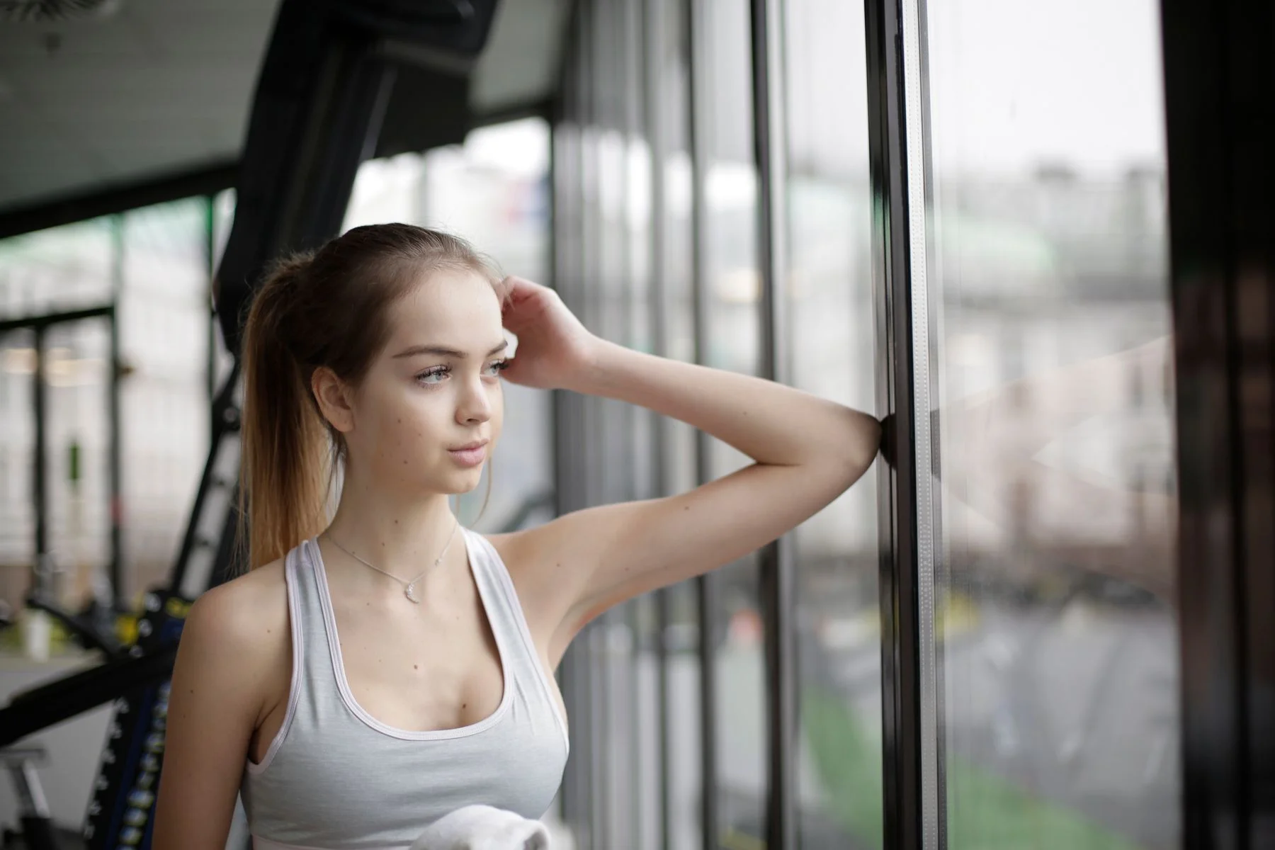 Woman standing pensively near a gym window, illustrating gym anxiety