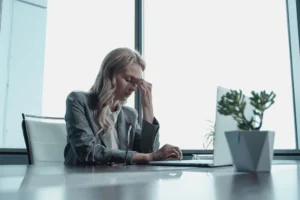 Woman pinching the bridge of her nose at her desk, stressed at work
