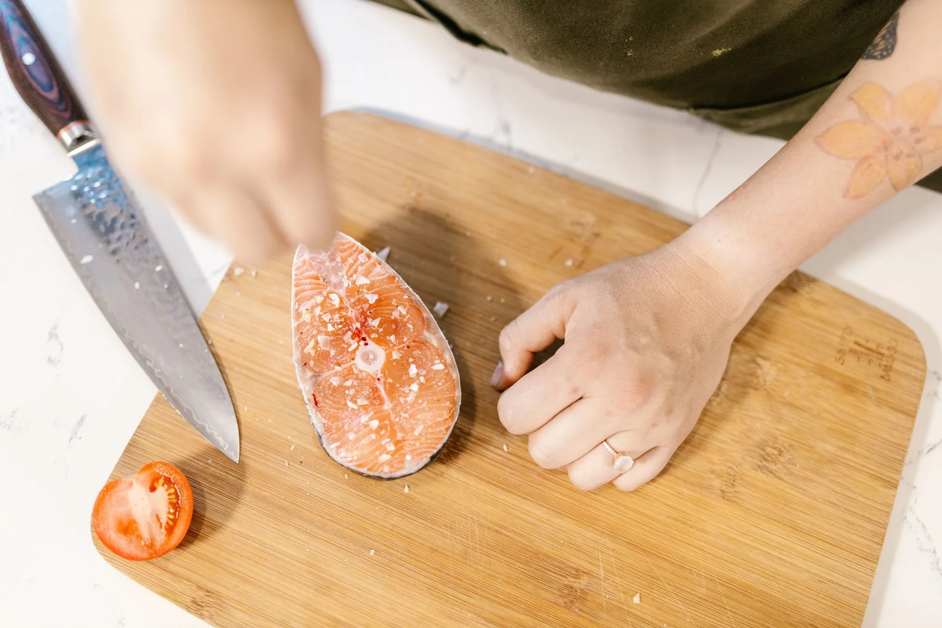 Raw salmon steak being salted on a wooden cutting board