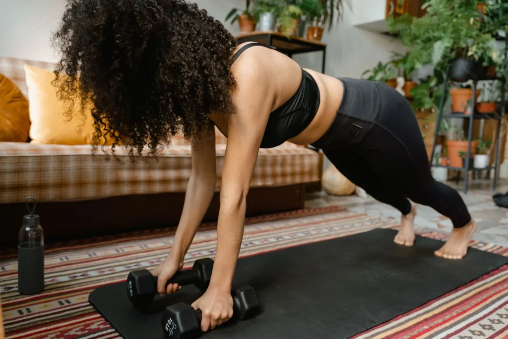 A woman doing a high plank on dumbbells on an exercise mat at home